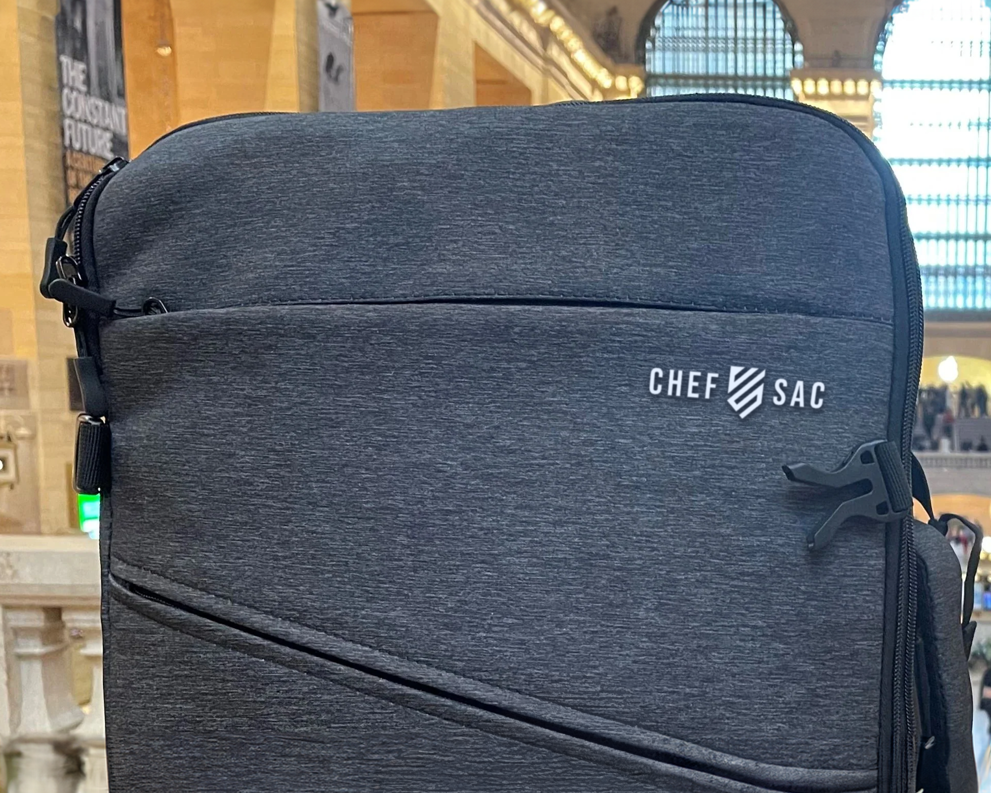 Heather black backpack with 'Chef Sac' logo in a blurred indoor setting