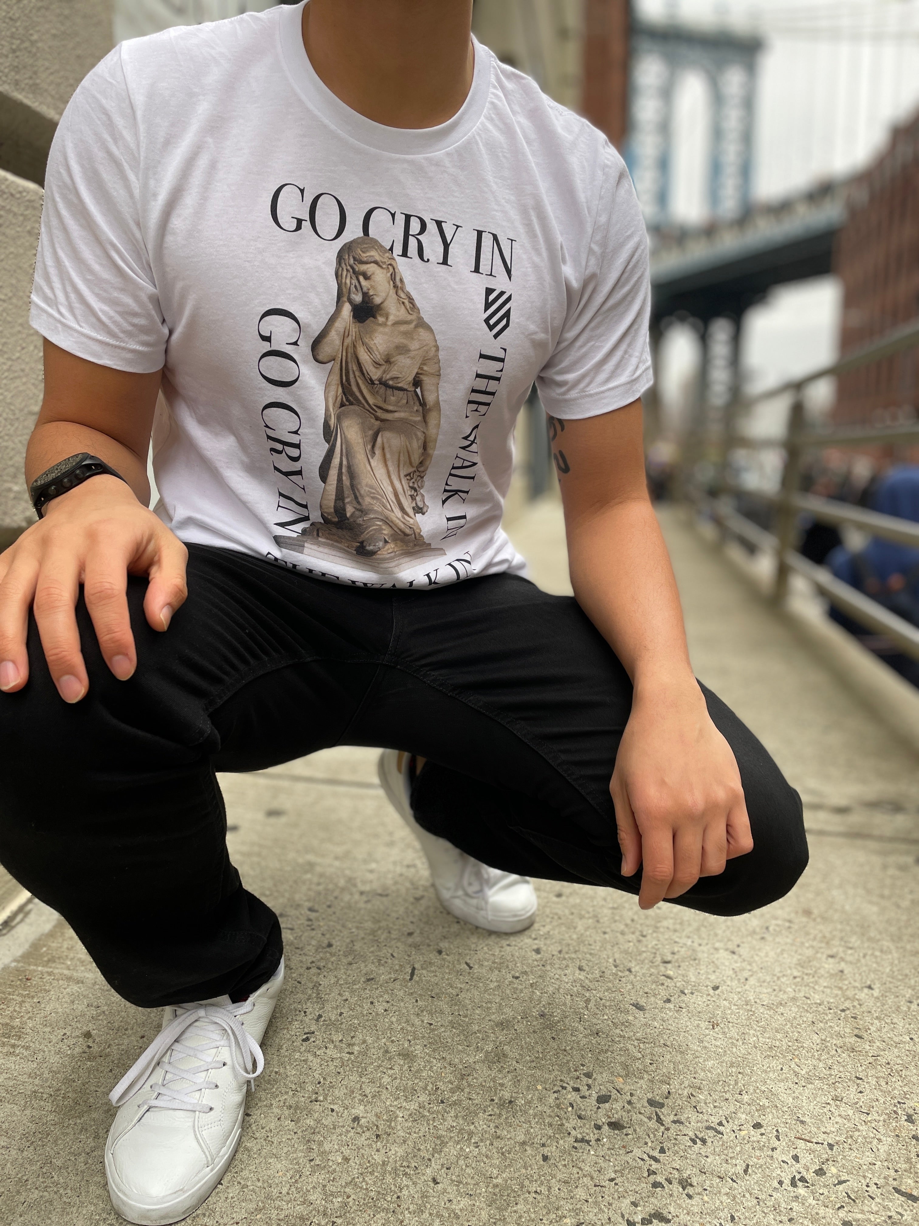 man crouched down with go cry in the walk in tshirt in city setting